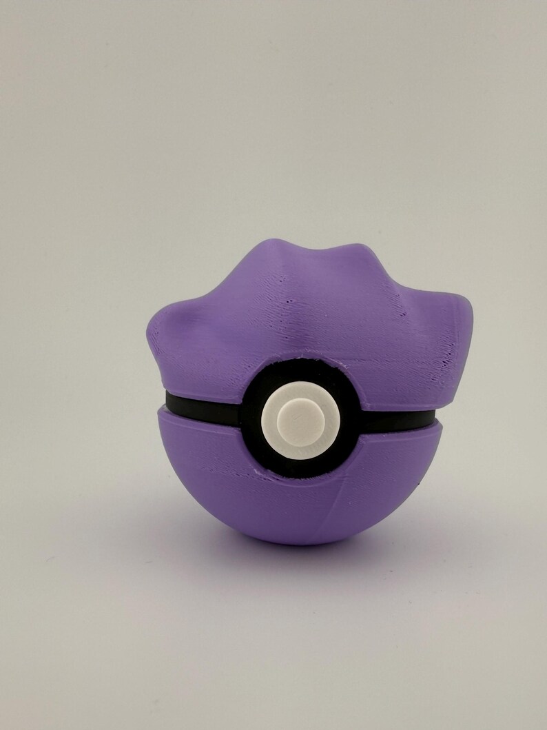 May include: A purple and black ball-shaped object with a white circular center. The top portion has a unique, curved design. The object is likely a toy or collectible item, possibly inspired by a popular animated series.