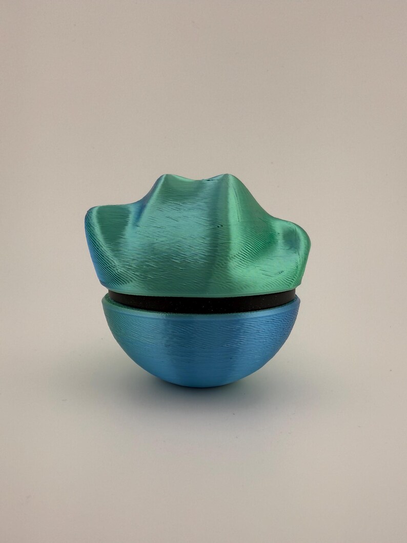 May include: A two-part, 3D-printed decorative object. The top section is a textured, teal-green color, resembling a stylized mountain range. The bottom section is a smooth, rounded shape in blue. A black band separates the two parts.