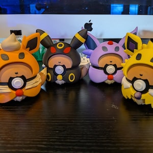 May include: Four colorful figurines in orange, black, purple, and yellow, each with unique ear and face designs. The figures have a round body with a white and black circular design on the front. The figurines are on a dark surface.