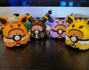 May include: Four colorful figurines in orange, black, purple, and yellow, each with unique ear and face designs. The figures have a round body with a white and black circular design on the front. The figurines are on a dark surface.