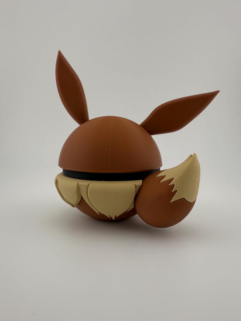 May include: A brown and tan Eevee figure, with large ears and a fluffy tail. The figure has a round body with a black band around the middle. The tail and the lower part of the figure are tan, while the rest is brown.