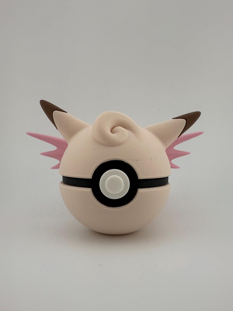 K&ouml;nnte beinhalten: Ein hellrosa und wei&szlig;er Pok&eacute;ball mit einem Cartoon-Charakter-Design. Die Figur hat braune Ohren, rosa Fl&uuml;gel und eine Wirbel auf der Oberseite. Der Ball hat einen schwarzen Streifen und einen wei&szlig;en Knopf.