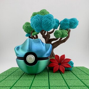 May include: A 3D-printed sculpture featuring a blue and green ball with a white button, a brown tree with green and blue foliage, and a red flower. The sculpture is set on a green, textured base.