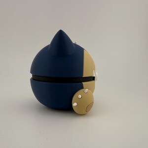 May include: A blue and tan spherical object with a pointed top and a small, round appendage. The object is split into two halves, with a black band separating them. The appendage has three white dots.