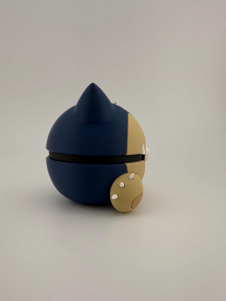 May include: A blue and tan spherical object with a pointed top and a small, round appendage. The object is split into two halves, with a black band separating them. The appendage has three white dots.