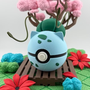 May include: A light blue and black decorative sphere with a white centre, resembling a character from a popular franchise. The sphere is set on a brown wooden platform, surrounded by red and blue floral accents, and a pink tree.