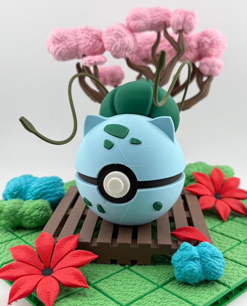 May include: A light blue and black decorative sphere with a white centre, resembling a character from a popular franchise. The sphere is set on a brown wooden platform, surrounded by red and blue floral accents, and a pink tree.