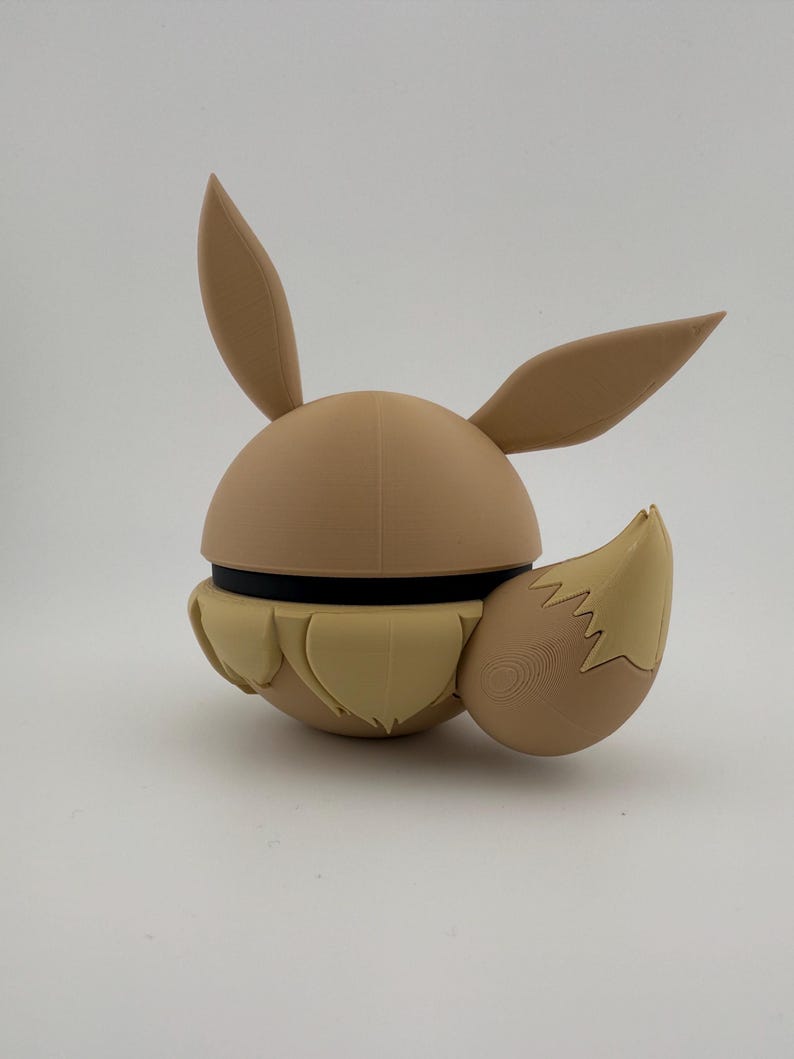 May include: A tan-coloured, 3D-printed figure of a cartoon character with large ears and a fluffy tail. The figure has a spherical body with a black band around the middle. The ears and tail are a lighter shade of tan.