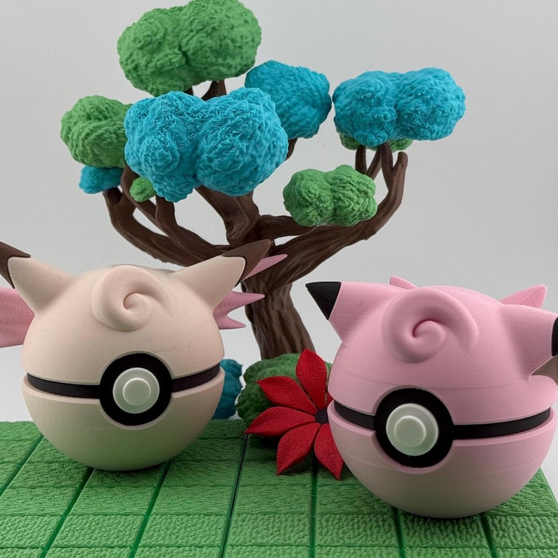 K&ouml;nnte beinhalten: Zwei rosa und wei&szlig;e Jigglypuff-Figuren mit schwarzen Akzenten, platziert auf einer gr&uuml;nen Plattform mit einem Miniaturbaum mit blauem und gr&uuml;nem Laub. Eine rote Blume befindet sich zwischen den Figuren. Der Hintergrund ist schlicht wei&szlig;.