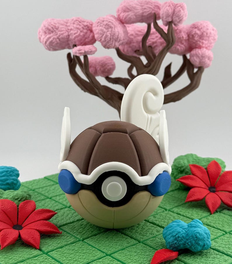 Pode incluir: Uma escultura detalhada e colorida de uma personagem de desenho animado com uma concha castanha segmentada, detalhes brancos e azuis. A personagem est&aacute; situada em um cen&aacute;rio de uma &aacute;rvore rosa, flores vermelhas e terreno verde.