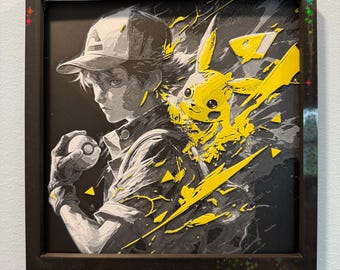 Op de afbeelding: Ingelijst kunstwerk met een grijswaarden illustratie van een persoon met een pet die een Poké Ball vasthoudt, met een felgele Pikachu die uit de zijkant barst. Het kunstwerk is geplaatst tegen een zwarte achtergrond en ingelijst in een donkerbruine lijst.