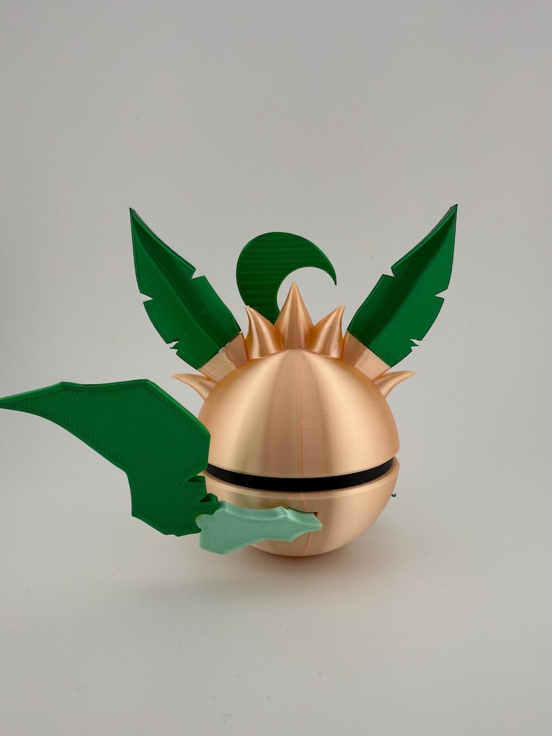 May include: A 3D-printed, spherical object with a metallic gold finish, featuring green leaf-like appendages and a spiky crown. A black band encircles the sphere. The design is reminiscent of a stylized plant or fruit.