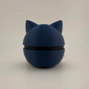 May include: A navy blue cat-shaped bottle stopper. The stopper is made of a smooth material and has a black band around the middle. The cat ears are pointed and stand upright. The product is designed to seal bottles.