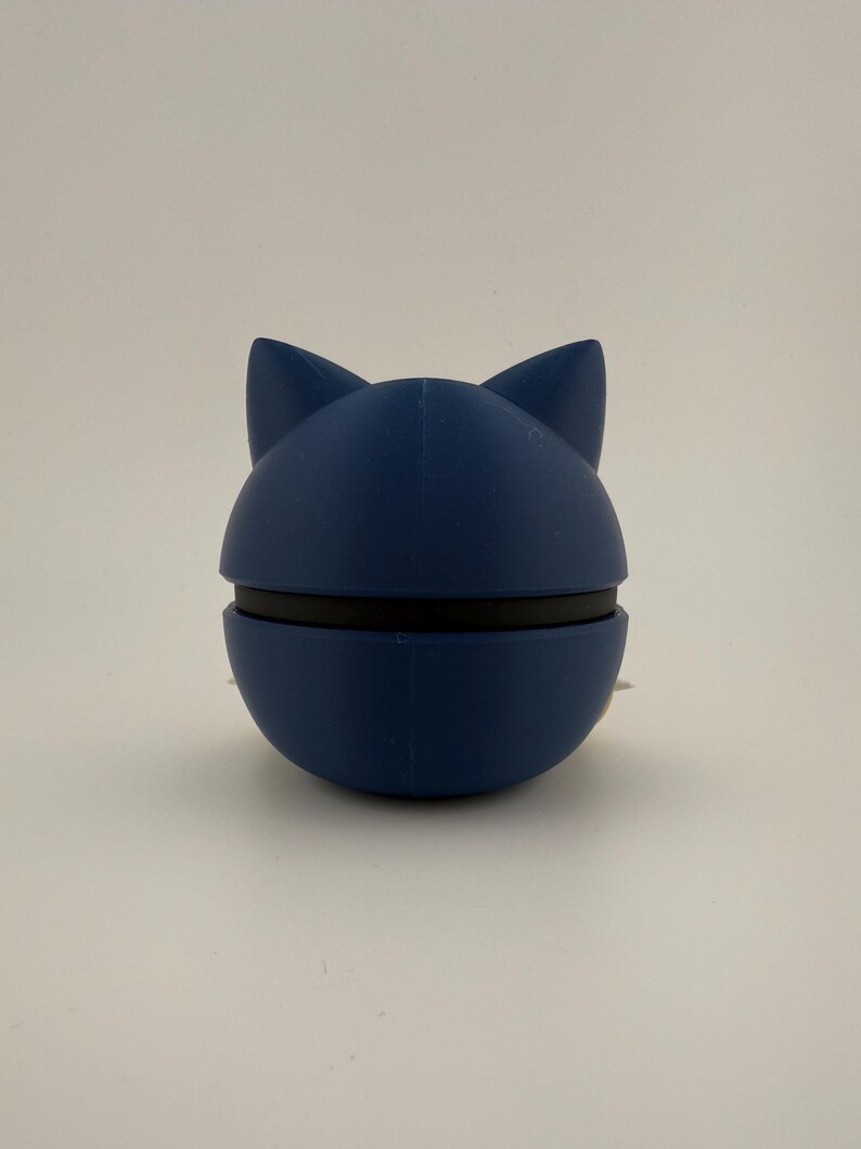 May include: A navy blue cat-shaped bottle stopper. The stopper is made of a smooth material and has a black band around the middle. The cat ears are pointed and stand upright. The product is designed to seal bottles.