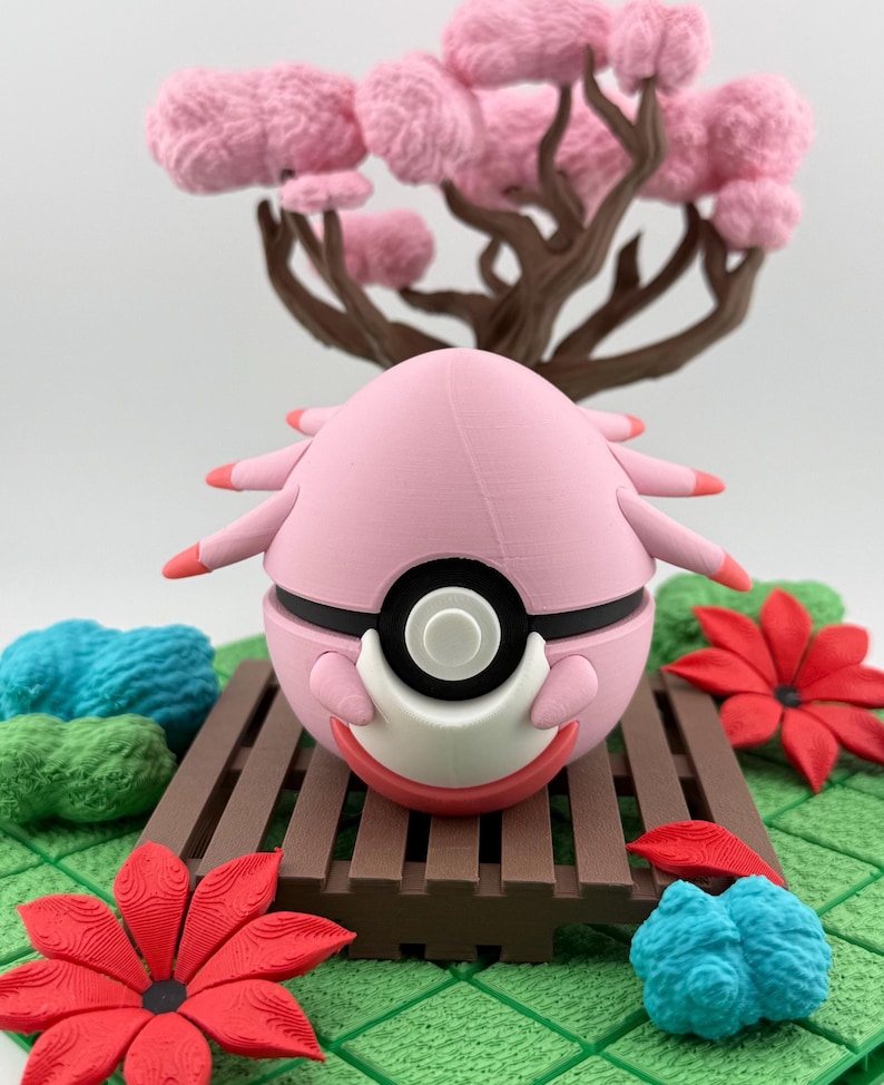 May include: A pink, spherical figurine with black and white accents, resembling a character from a popular animated series. It rests on a brown wooden platform, surrounded by red flowers, blue and green decorative elements, and a pink tree.