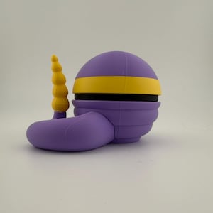 May include: A 3D-printed, stylized purple object with a yellow band and a yellow, segmented horn-like protrusion. The object has a rounded top and a curved, foot-like base. The design is geometric and smooth.