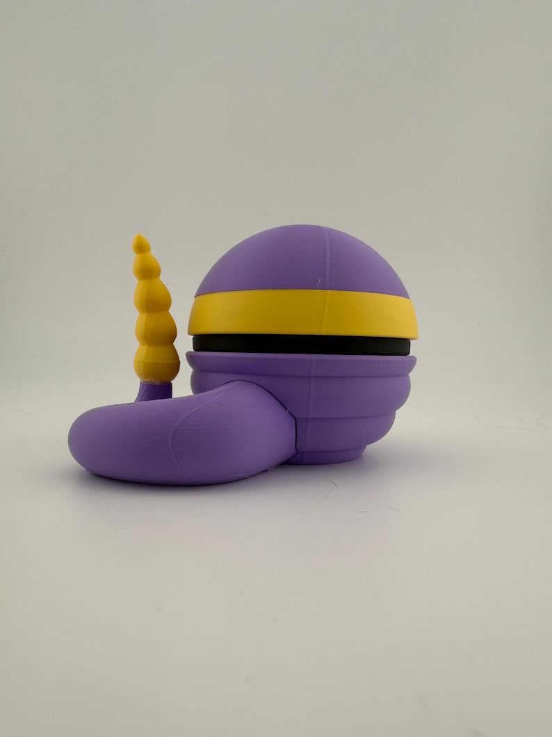 May include: A 3D-printed, stylized purple object with a yellow band and a yellow, segmented horn-like protrusion. The object has a rounded top and a curved, foot-like base. The design is geometric and smooth.