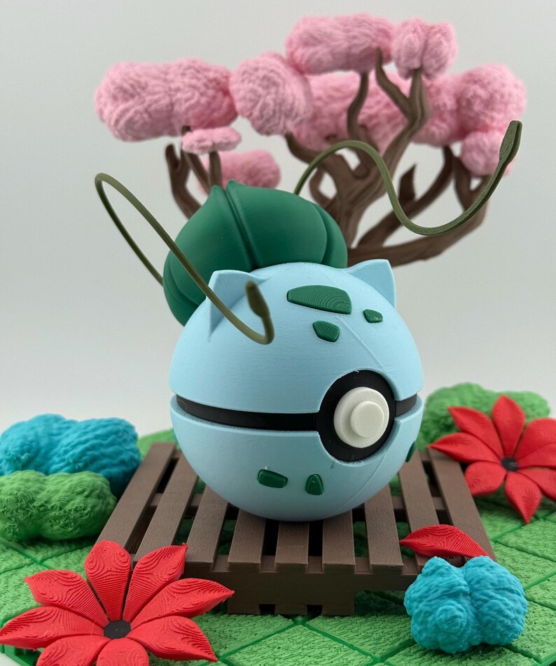 May include: A light blue, spherical figure with green details and a white centre, reminiscent of a popular character, rests on a brown wooden platform. The scene includes pink tree-like structures, red flowers, and green foliage.