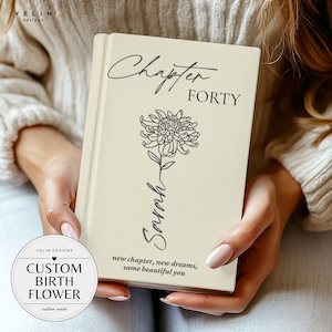 Peut inclure: Un livre à couverture rigide de couleur crème présentant le texte Chapter FORTY, une illustration au trait d'un chrysanthème, le prénom Sarah écrit en cursive et le texte new chapter, new dreams, same beautiful you sur la couverture.