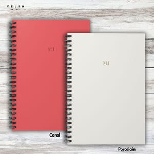 May include: Two spiral-bound notebooks, one coral and one porcelain, are displayed. The coral notebook is on the left, and the porcelain notebook is on the right. Both notebooks have the initials "MJ" in gold lettering. The word "Coral" is printed below the coral notebook, and "Porcelain" is printed below the porcelain notebook.