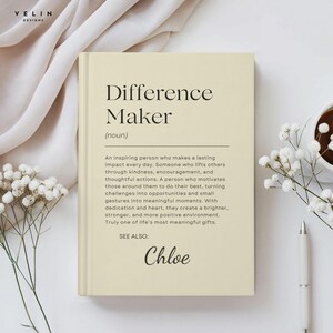 Może przedstawiać: Kremowa książka z czarnymi słowami "Difference Maker". Książka zawiera definicję i imię "Chloe" na dole. Książka otoczona jest białymi kwiatami, długopisem i filiżanką kawy.