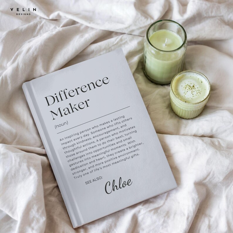 Może przedstawiać: Biała książka zatytułowana "Difference Maker" z definicją i imieniem "Chloe" jest wyświetlana na białym prześcieradle. Obok książki znajdują się dwa szklane pojemniki, jeden z zieloną świecą, a drugi z zielonym napojem.