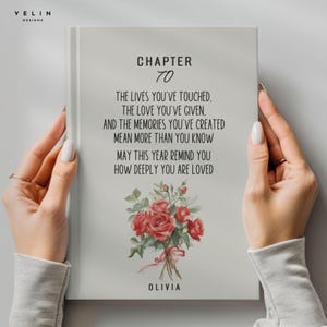May include: A light gray book cover with the text "CHAPTER 70" and a heartfelt message. Below the text is a watercolor bouquet of red roses. The name "OLIVIA" is printed at the bottom. The book is held by two hands.