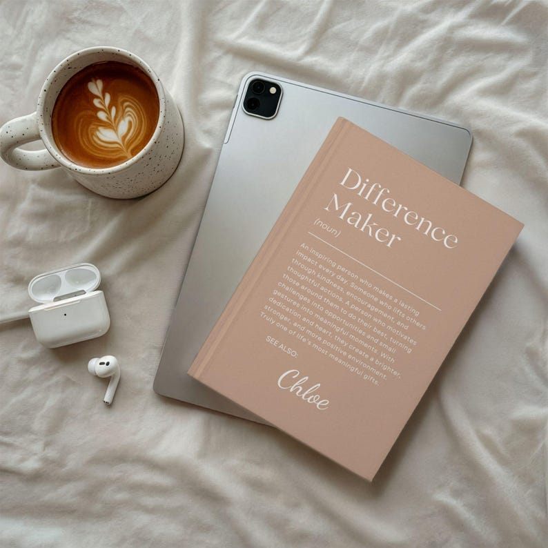Może przedstawiać: Jasnor&oacute;żowy notatnik z napisem "Difference Maker" i imieniem "Chloe" obok srebrnego tabletu, filiżanki kawy z latte art i pary białych bezprzewodowych słuchawek.