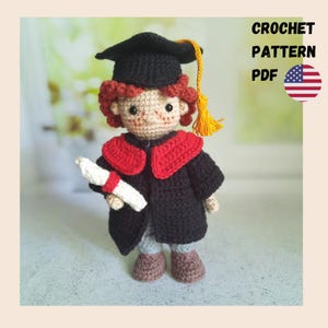 May include: Crochet pattern PDF for a graduation doll. The doll is wearing a black graduation gown with a red collar, a black graduation cap, and holding a scroll. The doll has red hair and a light brown face.