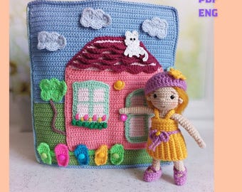 May include: A crocheted house-shaped pillow with a pink house, blue sky, and white clouds. A crocheted doll in a yellow dress and purple hat stands in front of the pillow. The pillow has the text "PATTERN PDF ENG".