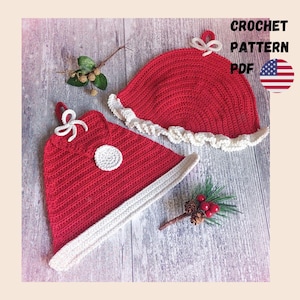 May include: Two red crocheted items with white trim and white bows, featuring the text CROCHET PATTERN PDF and a small United States flag icon. The items have a textured surface and are accompanied by small decorative pine sprigs with berries.
