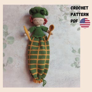 May include: Crocheted doll wearing a chef's hat and apron, holding a wooden spoon and knife. The apron is green with a yellow grid pattern. The text "CROCHET PATTERN PDF" is displayed with the American flag.