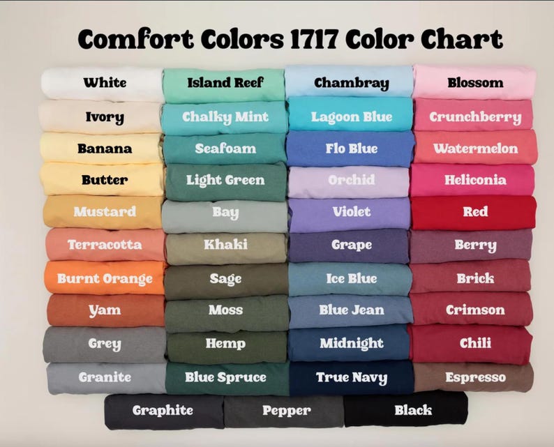 K&ouml;nnte beinhalten: Eine Comfort Colors 1717 Farbkarte mit achtundvierzig gefalteten T-Shirts in einem Raster. Jedes T-Shirt ist mit seinem spezifischen Farbnamen beschriftet, von Wei&szlig;-, Elfenbein- und Gelbt&ouml;nen bis hin zu verschiedenen Blau-, Gr&uuml;n-, Rosa-, Rot- und dunklen Neutralt&ouml;nen.