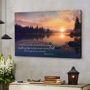 May include: A canvas print showing a sunset over a lake, with a vibrant sky of orange and purple. The artwork includes text from Psalm 121:1-2. The scene features trees and their reflections in the water, creating a tranquil atmosphere.