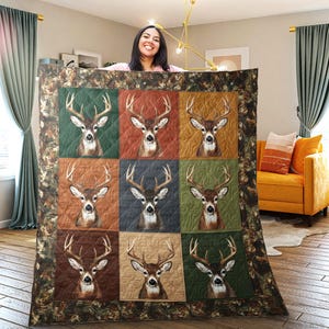 Puede incluir: Una manta acolchada con nueve cuadrados, cada uno mostrando una cabeza de ciervo con grandes astas sobre un fondo de diferente color. La manta tiene un borde de camuflaje y se muestra en interiores.