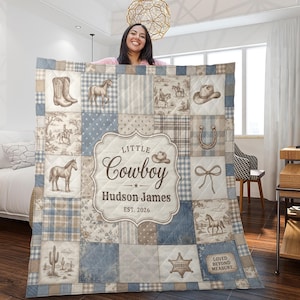 Puede incluir: Una colcha de patchwork en tonos azules y beige con ilustraciones de temática western que incluyen caballos, botas de vaquero, un sombrero, una herradura, un cactus y una insignia de sheriff. El texto central dice Little Cowboy, Hudson James, EST. 2026.