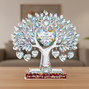 Puede incluir: Una escultura de árbol genealógico de cristal con un corazón central que dice "The Johnson Family". El árbol tiene hojas de cristal y colgantes en forma de corazón con nombres. La base dice: "Love makes a family, and Family makes a home."