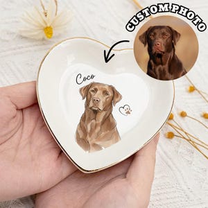 May include: A heart-shaped, white ceramic trinket dish with a gold rim. The dish features a custom illustration of a brown dog and the name "Coco". A circular image of the dog is also shown. The words "CUSTOM PHOTO" are above the image.