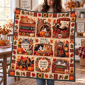 May include: A quilted throw blanket featuring a grid of autumn-themed illustrations including cats, pumpkins, fall leaves, and sunflowers. Text includes 'Thankful Hearts', 'Warm Paws', 'Gather & Give Thanks', 'Pumpkin Kisses', 'Michelle’s Home Is Where the Cats Are', 'Thankful Grateful Blessed', 'Good Food', 'Warm Cider', and 'Brighter Tomorrows'.