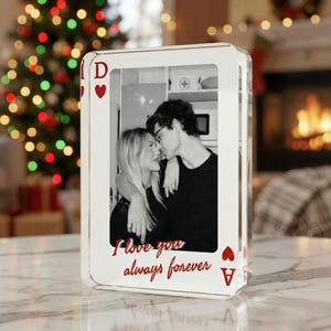 Puede incluir: Un marco de fotos transparente en forma de carta de juego de acrílico. Presenta una foto en blanco y negro de una pareja besándose. El marco tiene símbolos de corazón rojos y el texto "I love you always forever" en rojo.