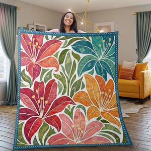 以下が含まれることがあります： 赤、オレンジ、ティール色の大きな花が白地に緑の葉で描かれた、花柄のブランケット。ブランケットは、青い縁取りにクロスステッチのデザインが施されています。