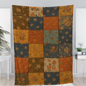 May include: A patchwork quilt with a floral pattern in shades of orange, blue, and yellow. The quilt is made of squares stitched together, creating a cosy and decorative textile. The quilt is a warm, inviting home decor item.