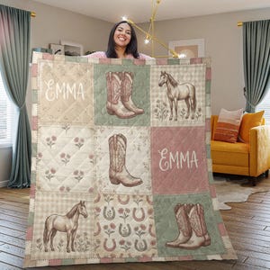 Op de afbeelding: Een doorgestikte plaid met een patchworkontwerp met illustraties van paarden, cowboylaarzen en hoefijzers in gedempte tinten saliegroen, oudroze en crème. De naam Emma staat in witte letters in twee van de vierkanten gedrukt.