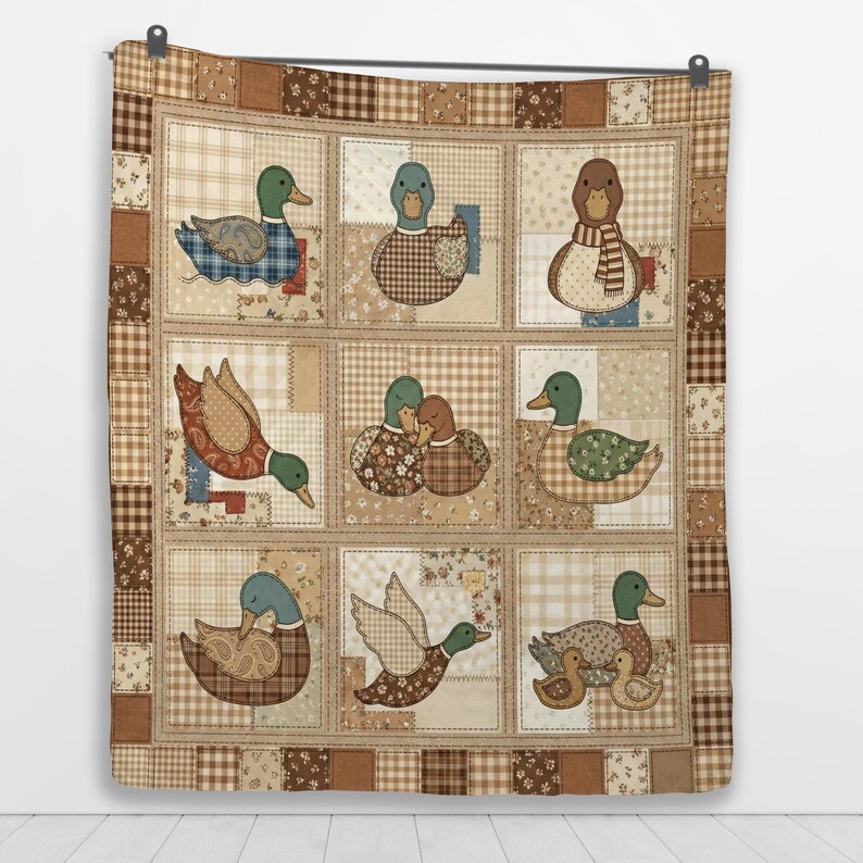 Puede incluir: Una colcha de patchwork con una cuadr&iacute;cula de nueve cuadrados, cada uno con una ilustraci&oacute;n de pato diferente. La colcha est&aacute; bordeada por cuadrados de tela a cuadros y florales en tonos marr&oacute;n y beige. Los patos tienen diversos patrones.