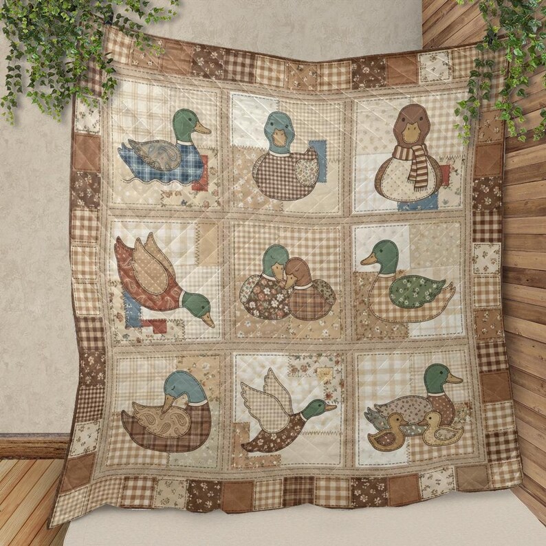 Puede incluir: Una manta acolchada con una cuadr&iacute;cula de nueve cuadrados, cada uno mostrando varios patos en tonos marr&oacute;n, beige y azul. Los cuadrados de tela usan patrones de cuadros, flores y s&oacute;lidos, con un borde de tela a cuadros marrones y beige.