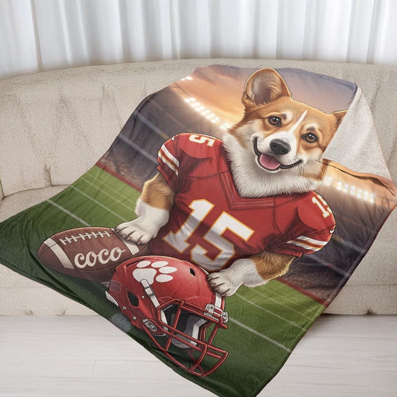 Puede incluir: Una manta acogedora con un corgi sonriente que lleva una camiseta de f&uacute;tbol roja con el n&uacute;mero 15. La manta tambi&eacute;n muestra un bal&oacute;n de f&uacute;tbol, un casco rojo con una huella de pata y un fondo de estadio. La palabra "coco" est&aacute; impresa en el bal&oacute;n.