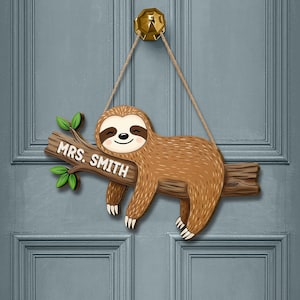 以下が含まれることがあります： 木製の枝に「MRS. SMITH」の文字が入った、茶色のナマケモノ型のドアサイン。 ナマケモノは笑顔でロープにぶら下がっており、枝には緑の葉が付いています。 サインは青いドアに掛けられています。