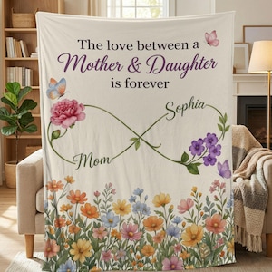 May include: Cream-colored blanket with floral and butterfly design. Text reads "The love between a Mother & Daughter is forever" with the names "Mom" and "Sophia". Features a colorful floral border.