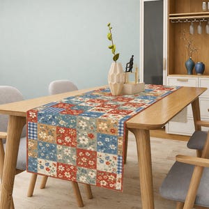 May include: A rectangular table runner with a patchwork design featuring squares of red, blue, and tan floral patterns. The runner is placed on a wooden table, adding a decorative touch to the dining area.