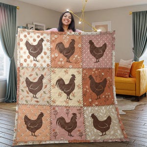Peut inclure: Une couverture patchwork avec des motifs de poulets et de coqs bruns sur des fonds floraux et à pois. La couverture est présentée dans une pièce avec un fauteuil jaune et des rideaux. Le design évoque un style champêtre.